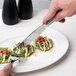 A hand holding a Libbey stainless steel dinner knife over a plate of food.