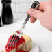 A Libbey stainless steel utility fork on a piece of cheesecake with cherry sauce.