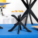 Black X-shaped Tablecraft risers on a blue table with a white tablecloth and a plate on it.