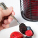 A hand holding a Libbey stainless steel teaspoon filled with berries.