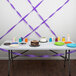 A table with purple streamers on it with a chocolate cake and cups.