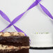 A chocolate cake with white frosting and a purple streamer on a table.