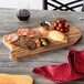 An American Metalcraft faux acacia melamine serving board with meat and cheese and grapes on a wood table.