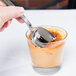 A hand holding a Libbey stainless steel dessert spoon over a glass of pudding.