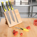 A Mercer Culinary Millennia knife set on a rubberwood magnetic board with yellow and black handles next to tomatoes.