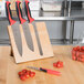 A group of Mercer Culinary Millennia knives with red handles on a Mercer Culinary wooden magnetic board next to tomatoes.