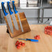 A Mercer Culinary wooden cutting board with a group of Mercer Culinary knives with blue handles on it.