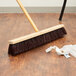 A Carlisle Flo Pac push broom head with maroon unflagged bristles on a wooden floor.