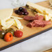 An American Metalcraft carbonized bamboo serving board with different types of cheese and olives on a table.
