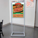 A silver Aarco double sided sign holder with a sign featuring a pizza.