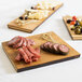 An American Metalcraft carbonized bamboo serving board with meat, cheese, and olives on a table with other wooden boards.