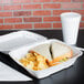 A sandwich and chips in a white foam container with a hinged lid.