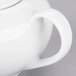 A white porcelain sugar bowl with a lid and handle on a white surface.