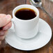A hand holding a 10 Strawberry Street Classic White espresso cup filled with coffee and a spoon.