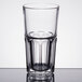 An Arcoroc stackable beverage glass filled with a clear liquid on a table.