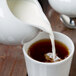 A 10 Strawberry Street white porcelain creamer pouring milk into a cup of coffee.
