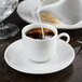 A white 10 Strawberry Street porcelain espresso cup and saucer with coffee being poured into it.