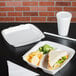 A white foam container with a sandwich and chips inside.