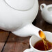 A white 10 Strawberry Street porcelain teapot pouring tea into a cup.