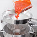 A person using a Vollrath china cap strainer to pour red sauce.