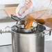 A person using a Vollrath fine china cap strainer to pour brown liquid into a pot.