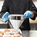 A chef uses a Vollrath Coarse China Cap Strainer to sprinkle powdered sugar on doughnuts.