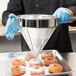 A person in a blue uniform using a Vollrath fine china cap strainer to pour powdered sugar on a donut.