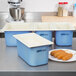 A white counter with blue Carlisle Coldmaster pans and white lids next to a plate of corn dogs.