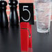 An American Metalcraft red clothespin card holder on a table with a number on it.