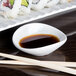 An Arcoroc oval porcelain bowl filled with soy sauce next to chopsticks on a table.