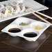 An Arcoroc white porcelain dish with four compartments filled with sushi, soy sauce, and sauces.