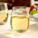 A clear, stemless wine glass filled with white wine, placed on a table.
