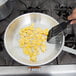 A person using a spatula to stir eggs in a Vollrath Arkadia aluminum fry pan.