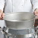 A person holding a silver Vollrath water pan with a handle.