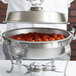 A person holding a Vollrath Royal Crest chafer water pan with meatballs in it.