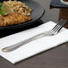 A 10 Strawberry Street Parisian gold stainless steel dinner fork on a napkin next to a plate of food.
