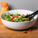 A CAC bright white porcelain salad bowl filled with salad with tongs.