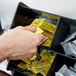 A person putting a packet of yellow paper into a black bin on a hotel buffet counter.