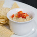 A white bowl of hummus with red peppers on top next to tortilla chips.