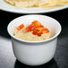 A white Cambro porcelain bowl filled with hummus and surrounded by red and orange food.