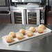 A MFG Tray eggshell fiberglass supreme display tray of muffins on a counter.