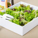 A Tablecraft white melamine bowl filled with salad on a table with a fork and spoon.