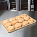 A MFG Tray Rattan Fiberglass Supreme Display Tray of doughnuts on a counter in a bakery display.
