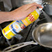 A hand using a PAM Buttercoat spray can to coat a pan on a stove.