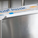 A silver Edlund stainless steel film and foil dispenser on a counter in a school kitchen.
