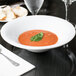 A Libbey aluma white porcelain soup bowl filled with soup on a table in an Italian restaurant.