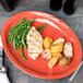 A Libbey Cantina Cayenne carved porcelain oval platter with chicken, potatoes, and green beans on a table.