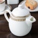 A white Syracuse China Baroque bone china teapot with gold trim on a table.