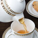 A Syracuse China Baroque bone china teapot pouring tea into a cup.