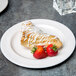 A pastry with white frosting and strawberries on a Libbey ivory porcelain plate.